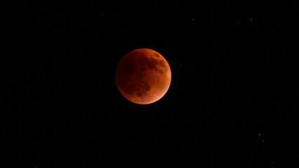 Blood moon during a lunar eclipse in the night sky. The moon appears red as it is shadowed by the Earth