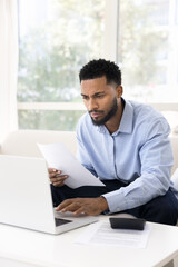 Serious young businessman engaged in domestic financial paperwork using notebook