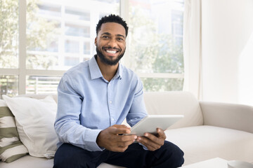 Portrait happy gen z man sitting on couch holding tablet