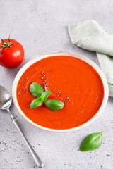 Vegetarian tomato cream soup with fresh basil on a gray background.