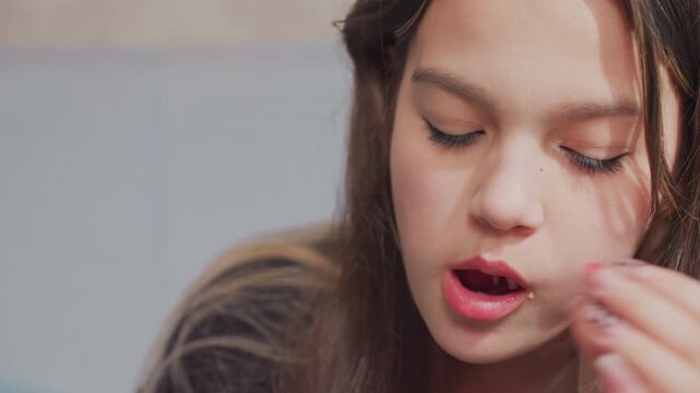 Close up side view of young girl eating potato chips with focused expression indoors, crumbs visible near mouth as she chews snack, showcasing natural behavior in casual, relaxed setting