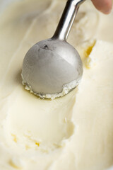 Vanilla ice cream scoop in metal spoon over creamy background, macro food texture shot