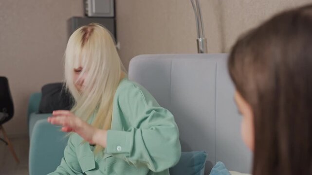 Girls engage in playful popcorn fight while sitting on bed in cozy room, blonde girl in green shirt raises hand to dodge incoming popcorn as friend teases her