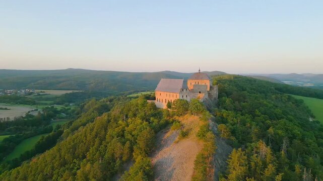 Experience the majestic beauty of Tocnik Castle as the sun sets over the hilltop. This medieval ruin offers stunning views surrounded by lush landscapes during a warm summer evening.