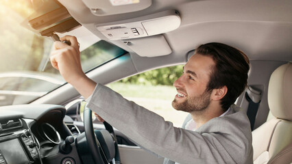 Man sitting in car and adjusting rearview mirror, car interior, road to office. Focused smiling caucasian handsome businessman looking into rear view mirror at auto at back seat, empty space, profile
