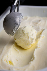 Vanilla ice cream scoop in metal spoon over creamy background, macro food texture shot