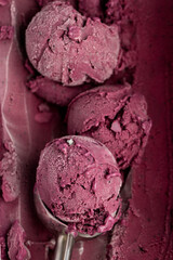 Scoop of vibrant berry sorbet in metal ice cream scooper, close-up, natural texture