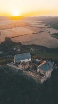 Witness the breathtaking views of Tocnik Castle as the sun sets behind the hills of Czechia. This medieval ruin stands proudly on a peak, surrounded by golden fields.