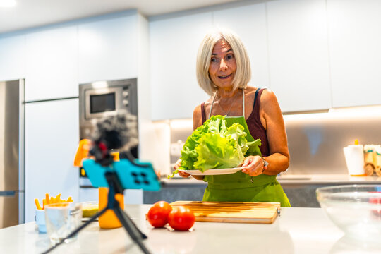 Mature woman filming cooking tutorial in modern kitchen