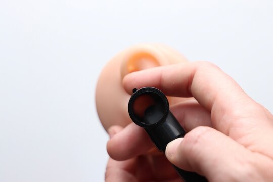 A person's hand uses a black otoscope to look inside a realistic model of a human ear, highlighting medical examination and anatomy study