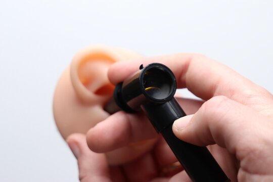 A person's hand uses a black otoscope to look inside a realistic model of a human ear, highlighting medical examination and anatomy study