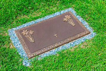 Bronze memorial marker with floral engravings cross rests on peaceful cemetery