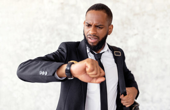 I'm Late. Portrait of worried African American businessman looking at wristwatch with open mouth with shocked facial expression, male wearing suit hurrying to work, rushing to office, selective focus - Powered by Adobe