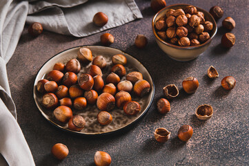 Nutritious unpeeled hazelnuts on a plate and peeled ones in a bowl on a table