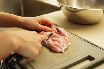 キッチンで生の鶏のもも肉を調理するために包丁で切っている女性