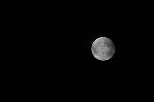 La lune partiellement visible dans un ciel nocturne tr&egrave;s sombre, avec des nuages fins obscurcissant l&eacute;g&egrave;rement sa surface, cr&eacute;ant une ambiance myst&eacute;rieuse et minimaliste. The moon partially visible