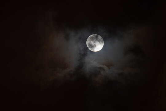 La pleine lune illumin&eacute;e &agrave; travers un ciel nocturne partiellement couvert de nuages sombres, cr&eacute;ant une ambiance myst&eacute;rieuse et dramatique.  Full moon shining through a partially cloudy night sky, cre