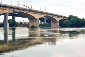 A sturdy concrete bridge arches elegantly over a flowing river, its clean geometric lines creating a striking contrast with the organic shapes of nature.