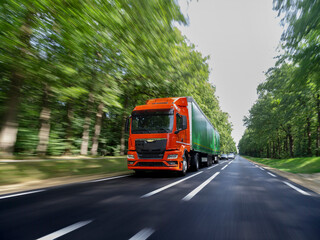 Orange truck with green trailer traveling at high speed with heavy motion blur on forest surroundings