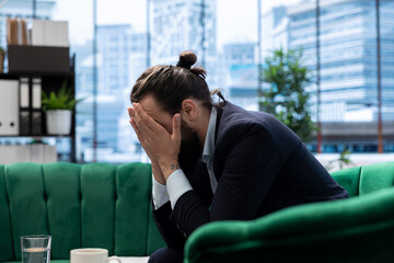 Male corporate leader buries his face in his hands due to frustration feeling the pressure of a...