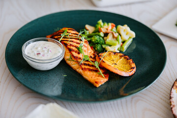 Grilled salmon fillet with vegetables, lemon and creamy sauce on elegant dark plate