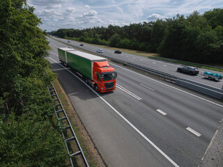 Orange truck with green trailer on multi-lane highway captured from elevated aerial perspective