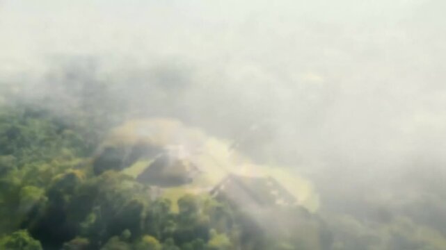 Aerial drone view of an ancient mayan pyramid temple complex nestled within a dense, lush green jungle forest, showcasing intricate stone architecture and surrounding vegetation