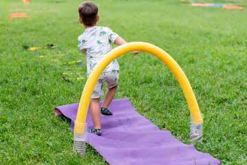 The boy overcomes an obstacle course. The child is playing on the green grass.
Sport and recreation concept.