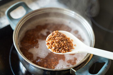 A spoon of buckwheat hovers over a pot of cooking grains, a superfood rich in nutrition. Ideal for food visuals, healthy recipes, or wellness lifestyle content with a wholesome appeal.