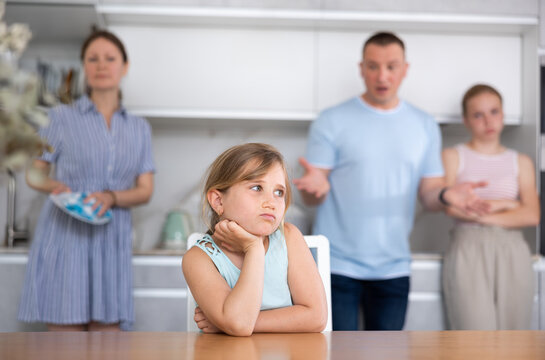 Parents scold child for bad behavior at school. Eldest daughter sits sullenly at table and listens to complaints from parents, edifying advice. Mom wipe dry dish in background