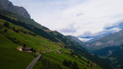 Swiss Alps with houses, winding road, clouds, and overcast sky, captured by drone. Schweizer Alpen mit Häusern, kurviger Straße, Wolken und bedecktem Himmel, aufgenommen mit Drohne.