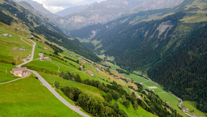 Swiss Alps with houses, winding road, clouds, and overcast sky, captured by drone. Schweizer Alpen mit Häusern, kurviger Straße, Wolken und bedecktem Himmel, aufgenommen mit Drohne.