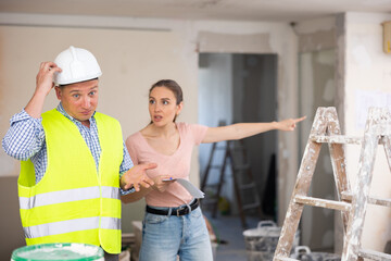 Portrait of perplexed man builder and annoyed gesturing woman, conflict between female architect and contractor at construction site of house being renovated
