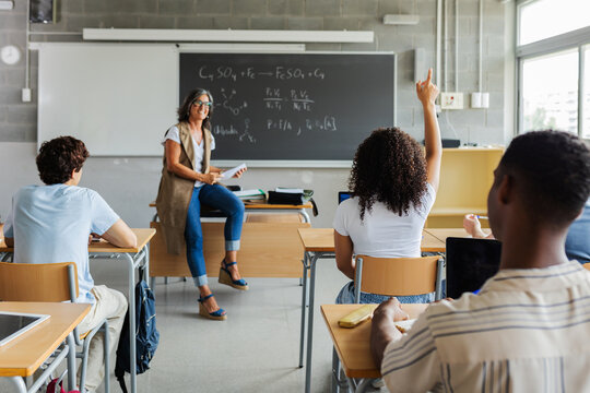 Rear view of young high school student girl raising her hand to ask a question in class. Education lifestyle and back to school concept - Powered by Adobe