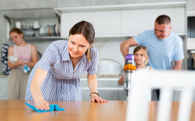 Obraz premium Mom is dusting the table. Father with children vacuuming the room