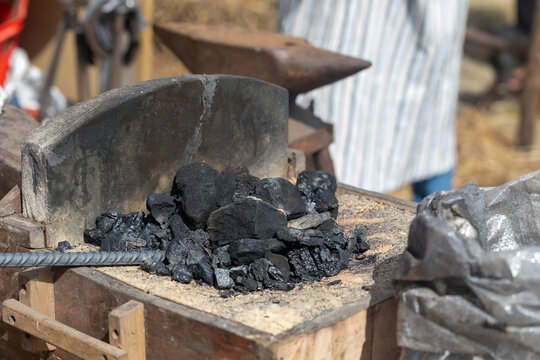 Blacksmith working with hot coal in the forge with metal rod and anvil in background - Powered by Adobe