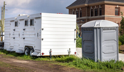 A plastic traditional portable toilet next to a luxury airconditioned toilet trailer at a...