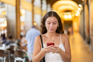 Young woman in summer clothes and with a phone in hands walks through the streets of Barcelona, she wants to meet friends and go to a restaurant in the evening