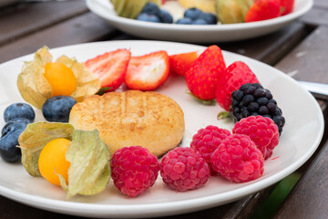 Fresh fruit platter featuring vibrant strawberries, blueberries, raspberries, and golden berries arranged beautifully on a white plate, showcasing healthy and energizing food options with copy space