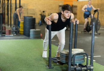Positive fit young European male in sportswear pushing heavyweight plates on prowler slider in...