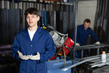 Young male worker in uniform posing with tape measure in metallurgical workshop