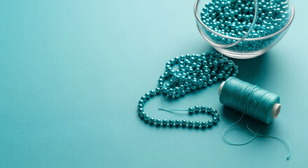 Turquoise pearls, glass bowl of beads, and thread spool, all on a blue backdrop