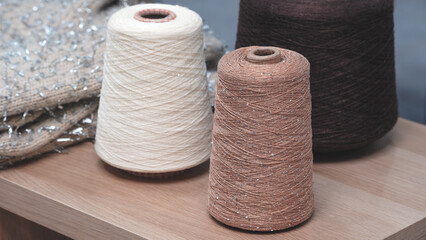 spools of thread are displayed on a wooden table. The spools are of different colors and textures, with one being a shiny gold and the other two being a cream color
