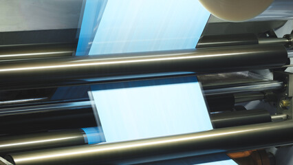 Roll of plastic film is being made in a factory. The roll is being fed into a machine that is cutting it into smaller pieces. The machine is surrounded by a metal frame