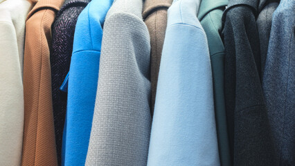 Row of coats hanging on a rack, with the blue coat being the most prominent. The coats are of...