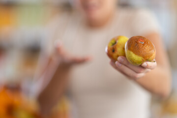 In store, blurred frustrated girl holds rotten fruits in hands, close-up. She accidentally took...
