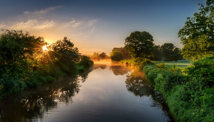 A Tranquil And Picturesque Scene Of A Stunning Sunrise Illuminating A Reflective Canal Embraced By Lush Greenery