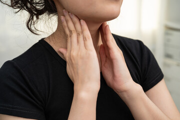 Asian woman touching her neck and throat for thyroid gland problem.