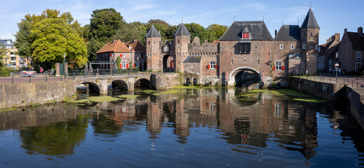 Wide angle panorama of the double gated medieval city entrance Koppelpoort structure reflecting in the Rijn canal water in the foreground on a sunny day