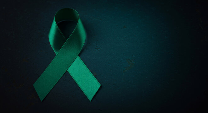 Green ribbon symbol on a dark background. Awareness ribbon concept representing mental health, glaucoma, and other causes